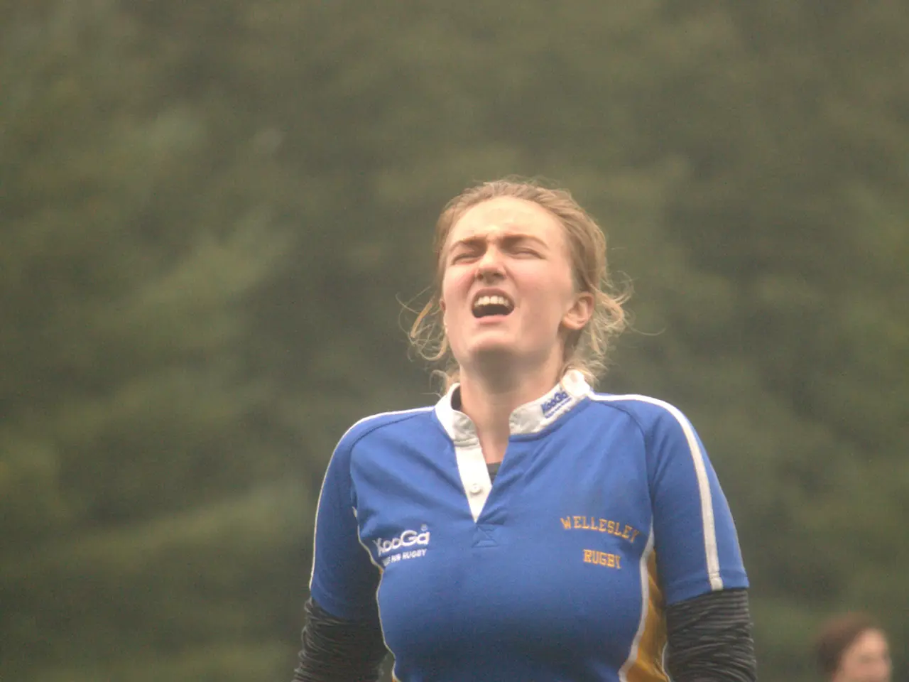 In this image we can see a woman wearing a rugby t shirt. The background is unclear and we can also...