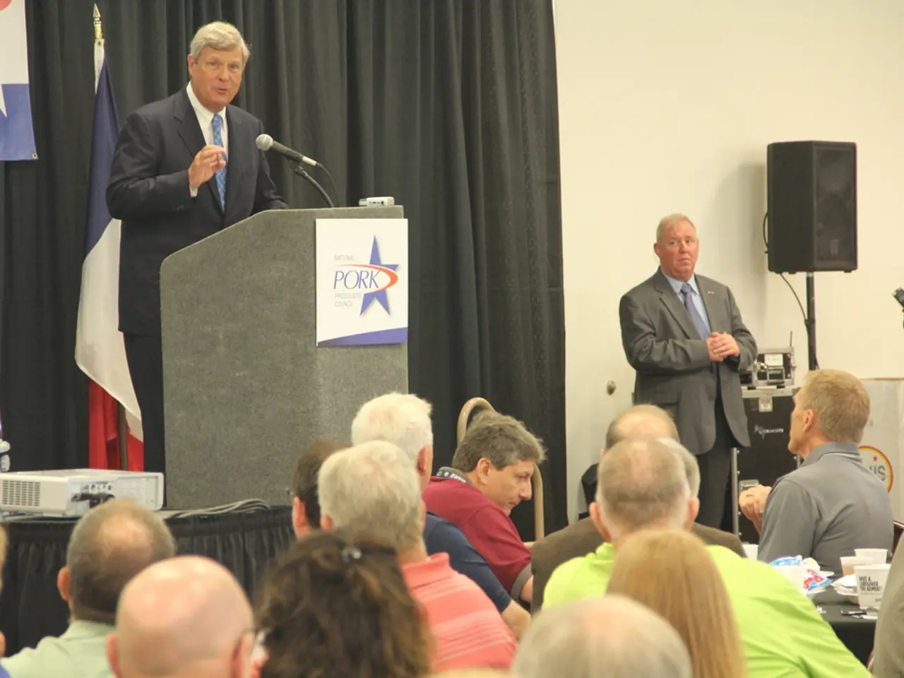 Here in this picture in the front we can see number of people sitting on chairs and we can see a...