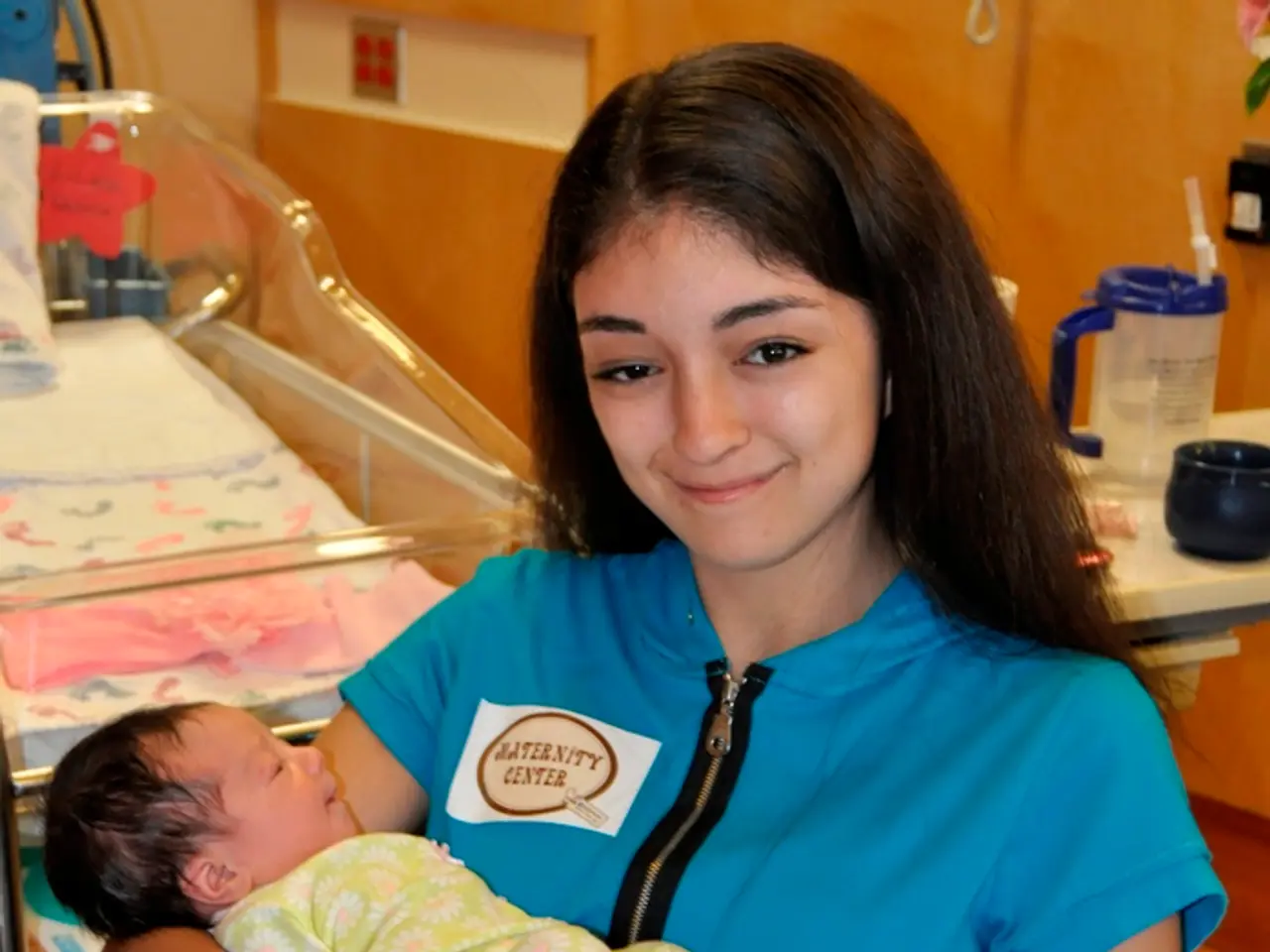 There is a woman in blue color t-shirt, holding a baby with both hands, smiling and sitting on a...