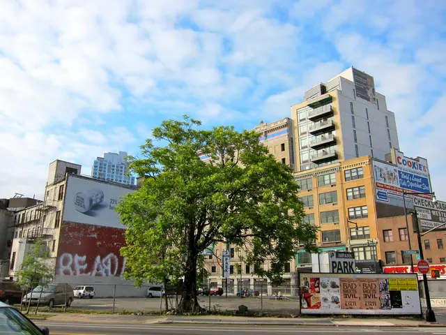 In this image there are many buildings. A street light and a tree. There is slightly cloudy and...