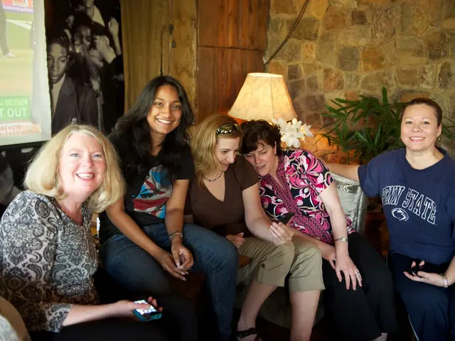 In this picture we can see five women sitting and smiling. In the background we can see the wall,...