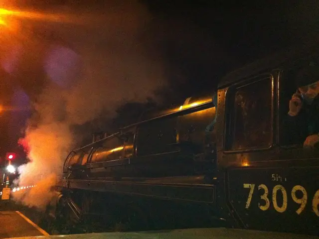 In this picture we can see a steam engine train on the railway track. The sky is dark.