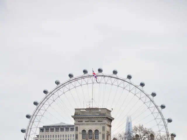 In this in front there is a fountain. In the background there are trees, buildings, flags and sky....