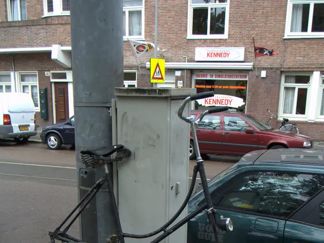 In this image I can see a bicycle. There are poles, name boards, vehicles, buildings, windows,...