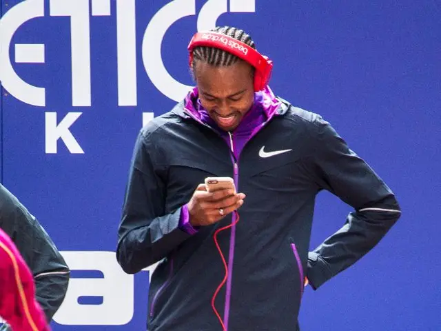 This is a person holding a mobile phone and standing. He is smiling. On the right side of the...