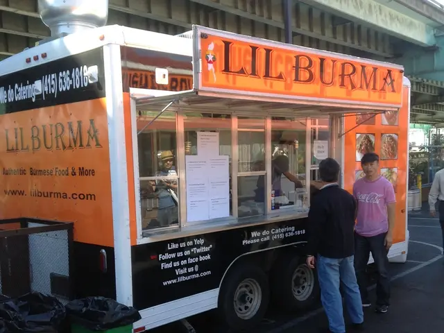 In this picture I can see buildings and few people standing and I can see a food truck and couple...