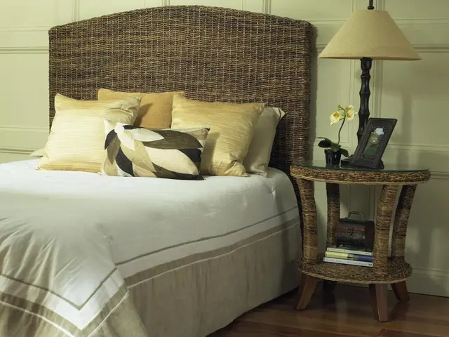 This picture shows a bed and few pillows and bed lamp and a photo frame and a plant and a table.